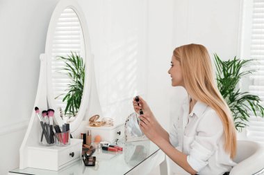 Güzel bir kadın aynanın yanında makyaj yapıyor.