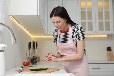 Mutfakta yemek pişirirken parmağını bıçakla kesen genç bir kadın.