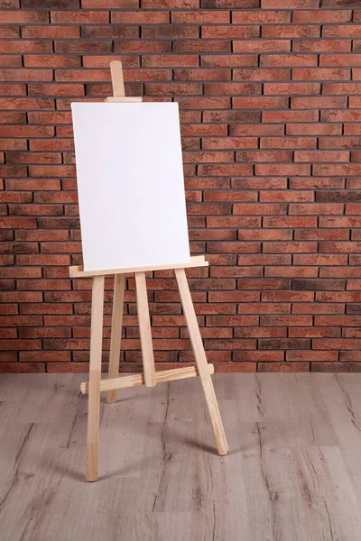 Wooden easel with blank canvas near brick wall