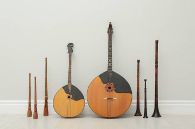 Beyaz duvarın yanında farklı ahşap müzik aletleri var.
