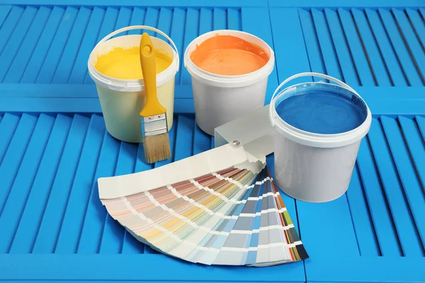 Buckets of paints, palette and brush on light blue wooden background
