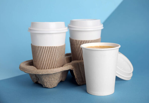 Takeaway paper coffee cups with sleeves, plastic lids and cardboard holder on blue background