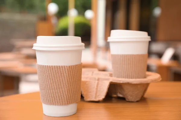 户外木制桌子上装有塑料盖子 袖子和纸板架的外卖咖啡杯 — 图库照片