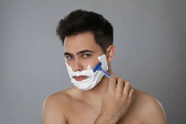 Joven Guapo Afeitándose Con Navaja Sobre Fondo Gris — Foto de Stock