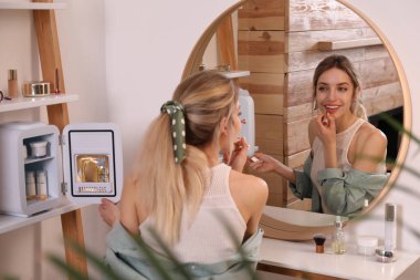 Kozmetik buzdolabının yanında ruj kullanan bir kadın.