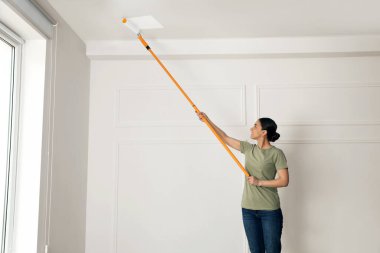 Tavanı beyaz boyayla boyayan genç bir kadın.