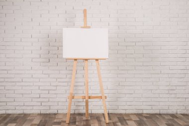 Beyaz tuğla duvarın yanında boş tuval olan ahşap sehpa