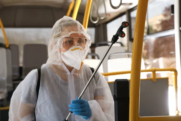 Public transport sanitation. Worker in protective suit disinfecting bus salon, focus on spray machine nozzle