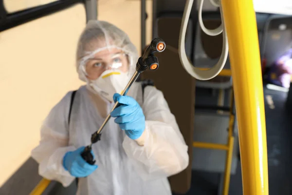 Public transport sanitation. Worker in protective suit disinfecting bus salon, focus on spray machine nozzle