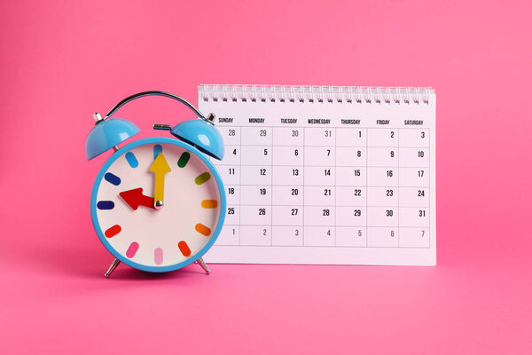 Будильник и календарь на розовом фоне. Концепция напоминания