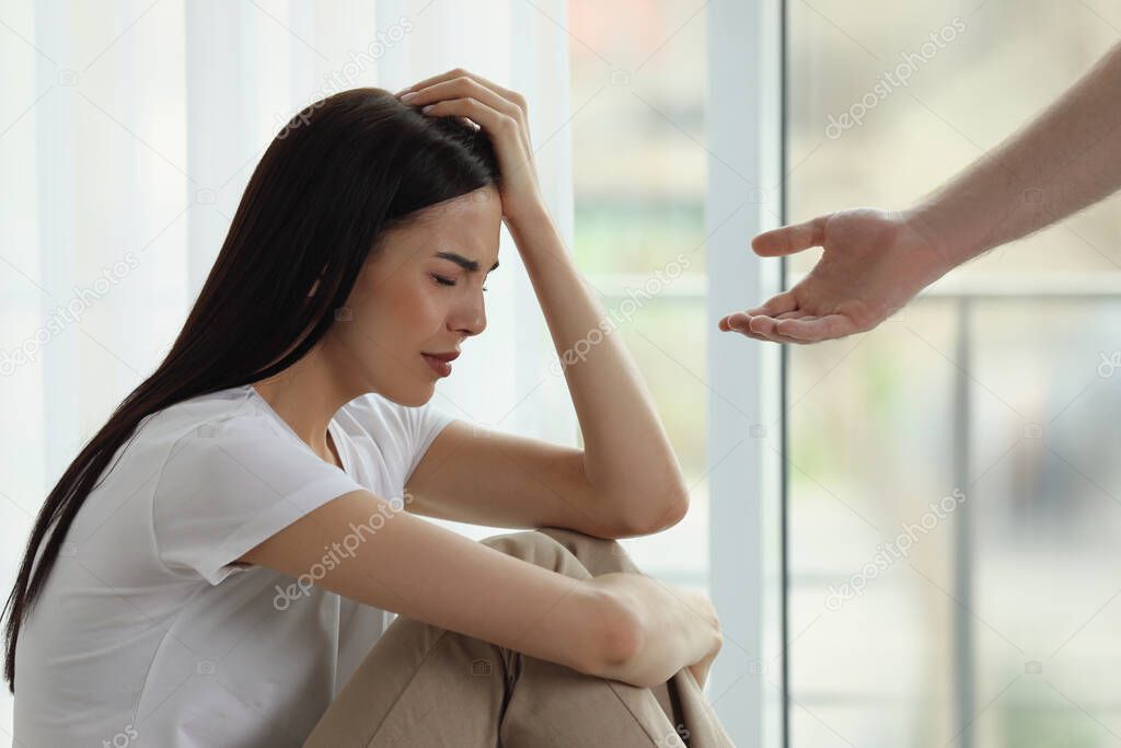 Man offering hand to depressed woman indoors