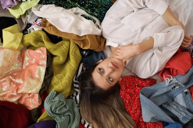 Farklı kıyafetlerin üzerinde yatan genç bir kadın. Hızlı moda konsepti