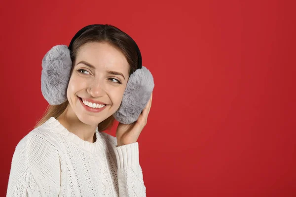 赤い背景に暖かい耳飾りを身に着けている幸せな女性 テキストのためのスペース — ストック写真