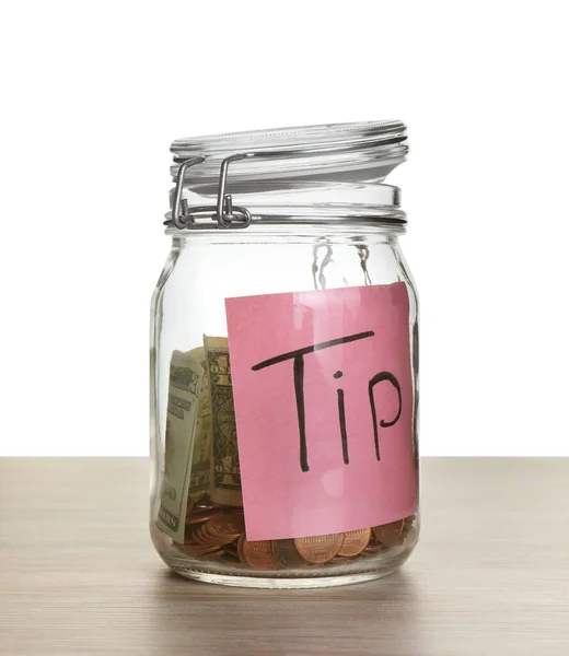 Tip jar with money on wooden table against white background