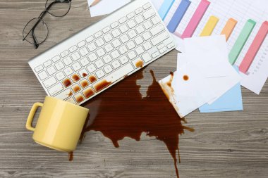 Bir fincan kahve, ahşap ofis masasındaki bilgisayar klavyesinin üzerine döküldü.