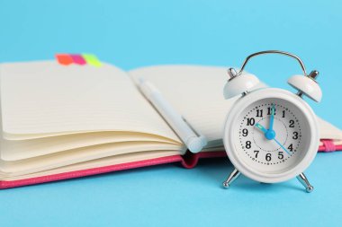 Alarm saati, kalem ve açık mavi arka planda bir defter. Hatırlatma konsepti