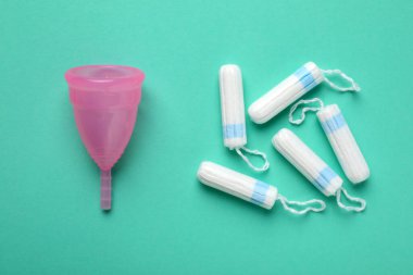 Turkuaz arka planda regl bardağı ve tamponlar, düz yatış.