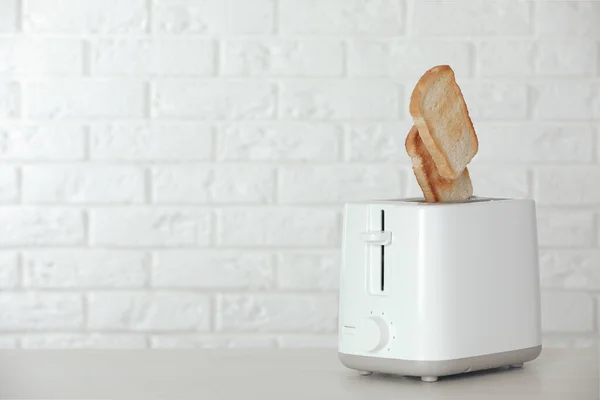 Bread slices popping up out of electric toaster on wooden table. Space for text