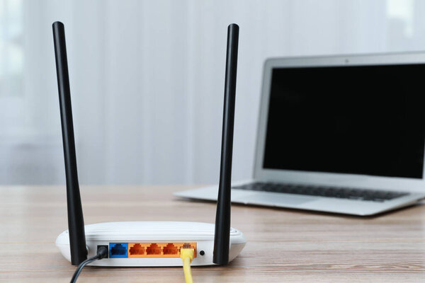 Modern Wi-Fi router and laptop on wooden table indoors