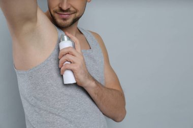 Gri arka plana deodorant süren adam, yakın plan. Metin için boşluk