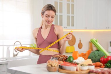 Elinde mezurası ve mutfakta farklı ürünleri olan bir kadın. Keto diyeti