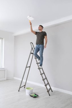 Merdivende merdivenle tavanı boyayan bir adam var.