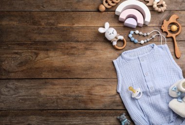 Tahta arka planda bebek kıyafetleri ve aksesuarlarıyla düz kompozisyon, metin için boşluk