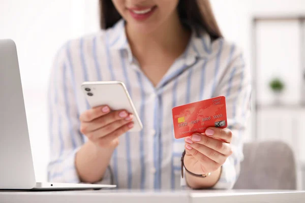 Woman with credit card using smartphone for online shopping at white table, closeup