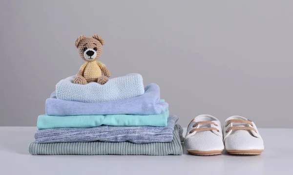 明るい灰色の背景に対してテーブルの上にきれいな赤ちゃんの服 おもちゃ 小さな靴のスタック テキストのスペース — ストック写真