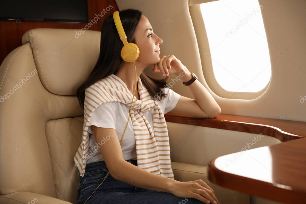 Young woman with headphones listening to music in airplane during flight