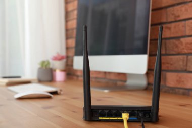 Tahta masadaki bilgisayarın yanında modern Wi-Fi yönlendirici