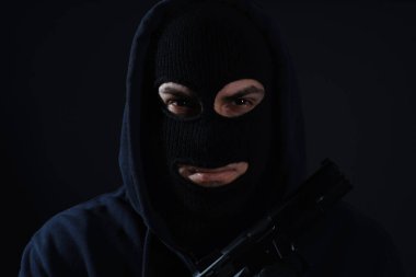 Siyah arka planda silahlı, örülmüş kar maskesi giyen bir adam.