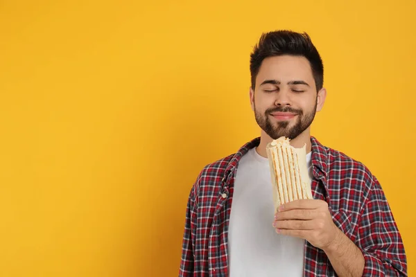 若い男は黄色の背景においしいシャワルマを食べる テキストのスペース — ストック写真