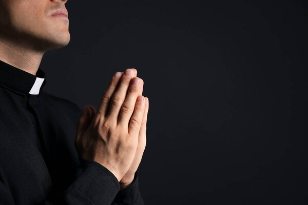 Priest praying on black background, closeup. Space for text