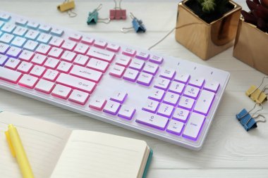 Beyaz ahşap masa üzerinde modern RGB klavye ve ofis kırtasiyesi