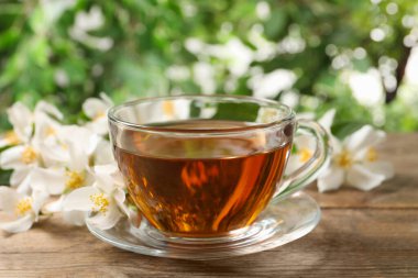 Cam bardakta aromatik yasemin çayı ve ahşap masada taze çiçekler, yakın plan.