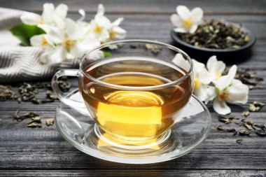 Bir bardak aromatik yasemin çayı ve siyah ahşap masada taze çiçekler.