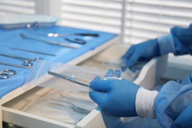 Doktor kapalı çekmeceye tıbbi forseps koyuyor, yakın plan. Farklı cerrahi gereçleri olan masa