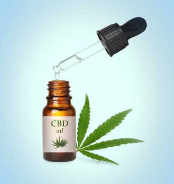 Bir şişe cannabidiol tentürü ve açık mavi arkaplanda kenevir yaprağı.