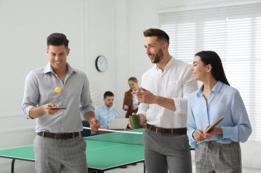 Ofisteki masa tenisi masasının yanında iş adamları konuşuyor.