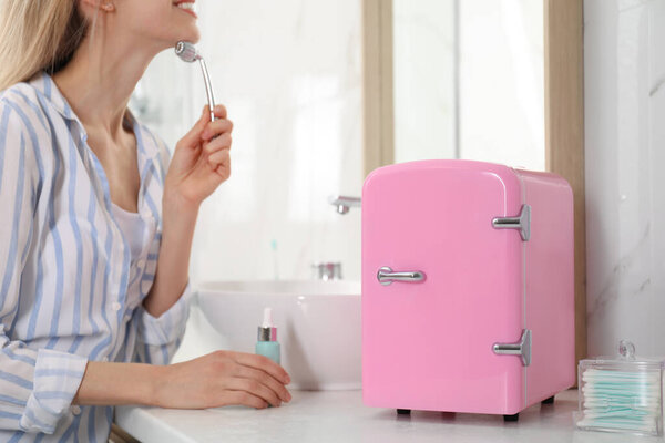 Женщина с металлическим катком для лица возле косметического холодильника в ванной, крупным планом