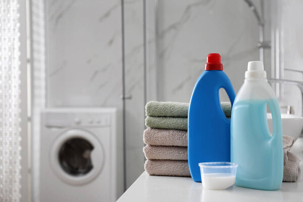 Stack of folded towels and detergents on white table in bathroom, space for text