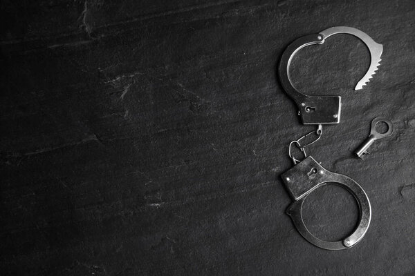 Classic chain handcuffs with key on black table, flat lay. Space for text