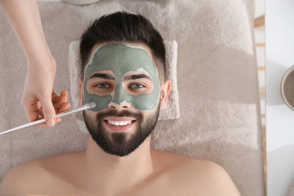 Cosmetologist applying mask on man\'s face in spa salon, top view