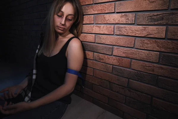 Overdosed drug addicted woman near brick wall. Space for text