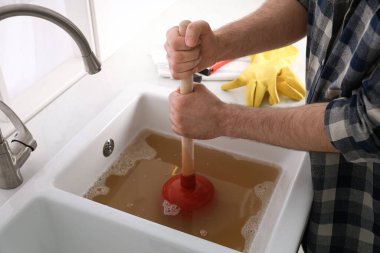 Lavaboyu açmak için lavabo pompası kullanan adam mutfaktaki gideri kapatıyor.
