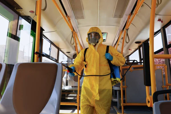 Public transport sanitation. Worker in protective suit disinfecting bus salon