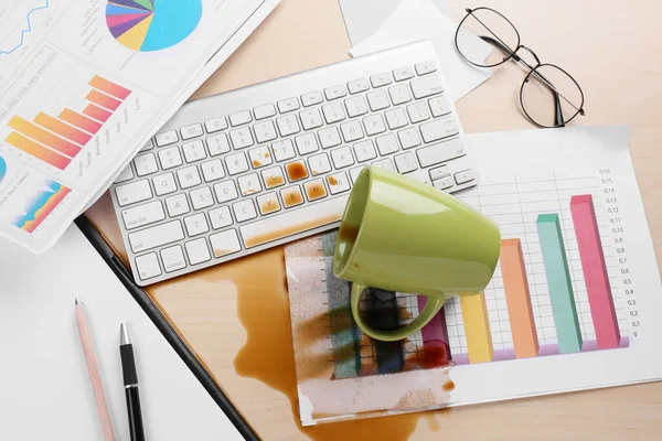 Cup of coffee spilled over computer keyboard on wooden office desk, above view