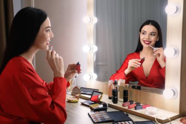 Güzel bir kadın aynanın yanında makyaj yapıyor.