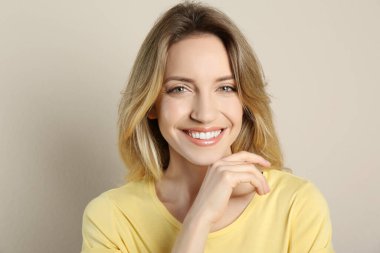 Güzel sarı saçları ve bej arka planda büyüleyici gülümsemesi olan mutlu genç bir kadının portresi.
